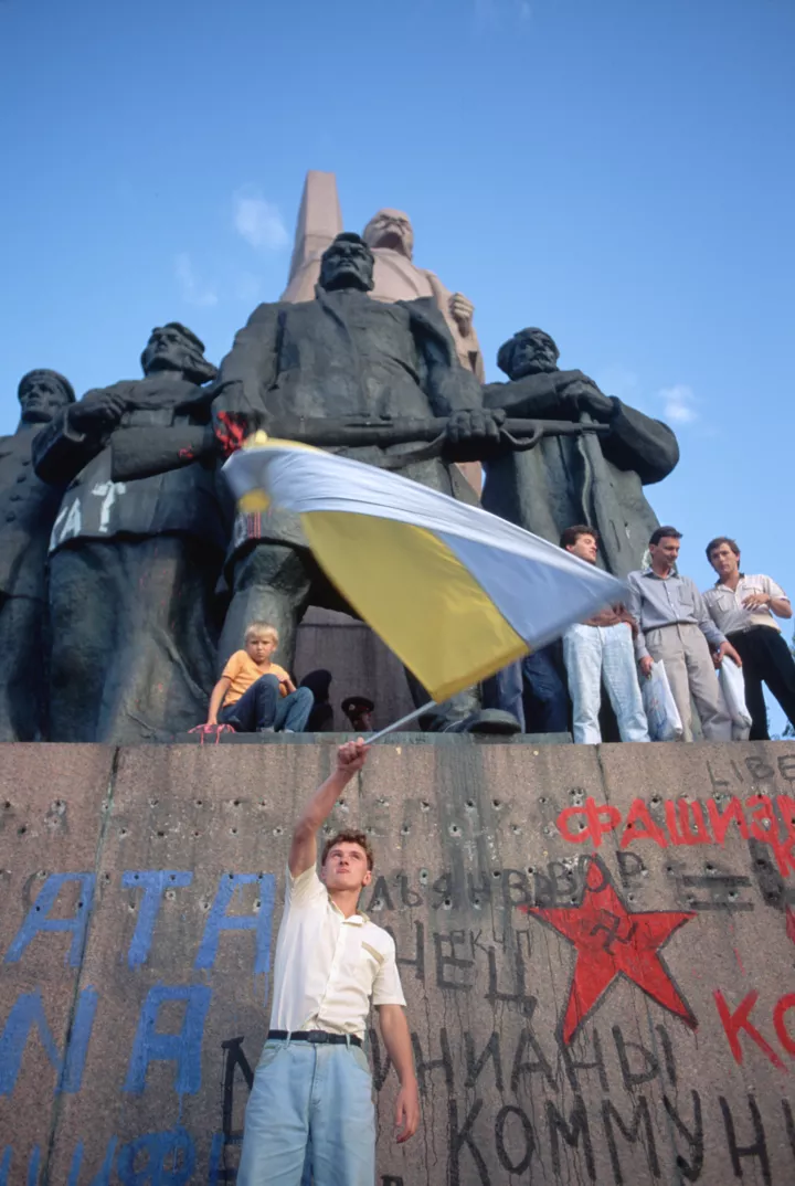 Чоловік з українським прапором поруч зі статуєю Леніна, на яку нанесли антикомуністичні гасла, 1 вересня 1991 року