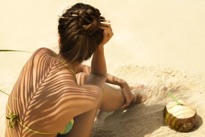 Девушка на пляже загорает в купальнике под пальмой.